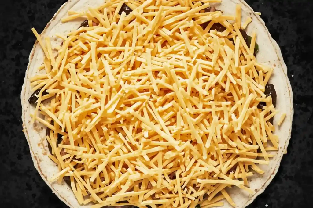 Freshly shredded cheddar cheese added to a tortilla for making crispy homemade cheese quesadillas