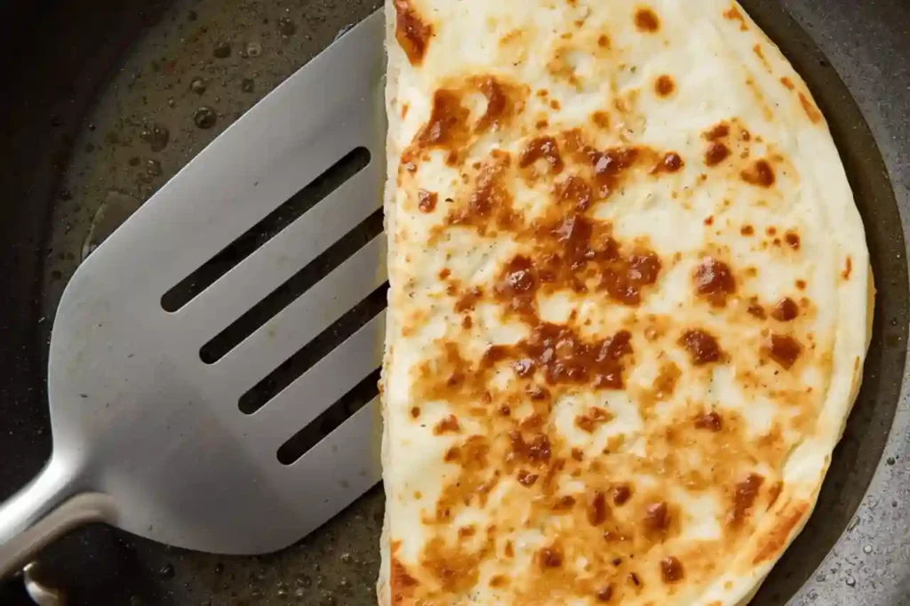 Golden crispy cheese quesadilla being flipped carefully in a skillet with a spatula for even browning and melted cheese inside