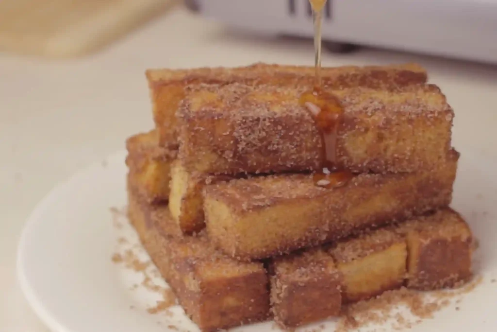 Mini French toast sticks stacked on a plate with cinnamon and golden crispy texture