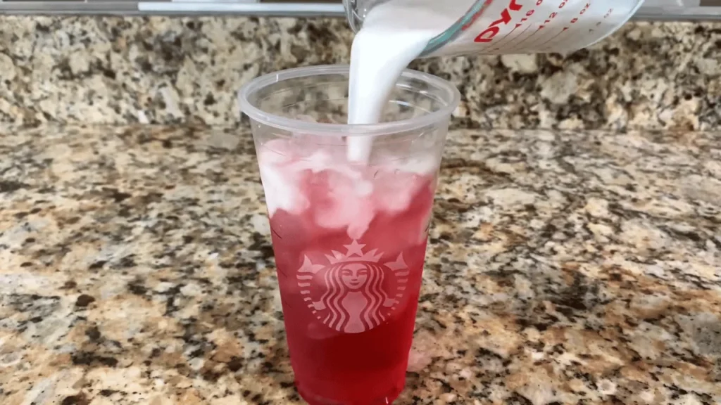 Coconut milk being poured into a strawberry refresher drink with ice to create a homemade pink drink
