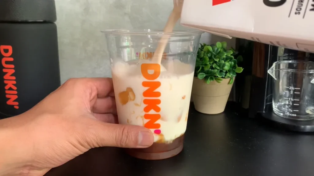 Adding milk to a Dunkin iced coffee for a homemade viral coffee drink recipe