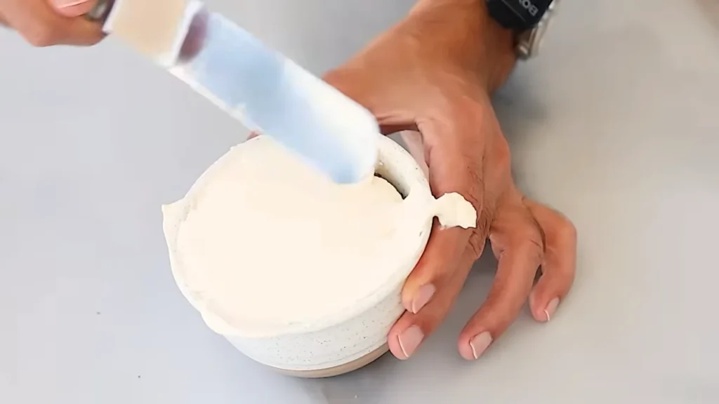 Applying smooth buttercream frosting to a vanilla cake before adding decorative frosting dots