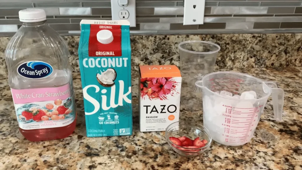 Coconut milk, Tazo tea, and measuring cups arranged on a kitchen counter for preparing a homemade beverage