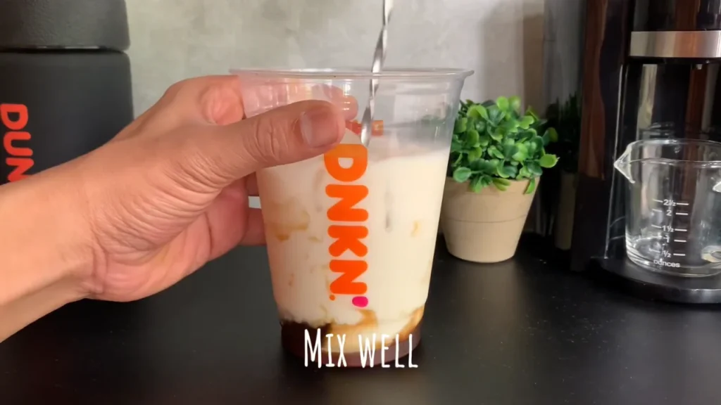Mixing caramel and vanilla syrup in a Dunkin cup for a viral coffee drink recipe
