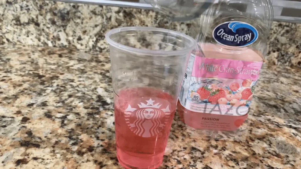 Strawberry drink base being prepared in a clear cup on a kitchen countertop with strawberry refresher concentrate bottle