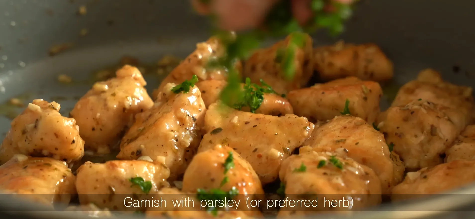Garnishing freshly cooked garlic butter chicken with finely chopped green parsley in a pan