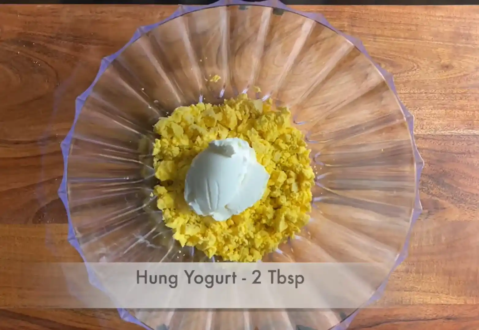 Adding 2 tablespoons of thick hung yogurt to egg yolks in a glass bowl