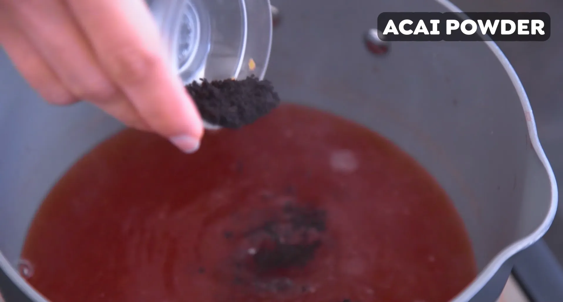 Adding pure acai powder into warm strained strawberry juice base in a pot to create dark purple acai flavor