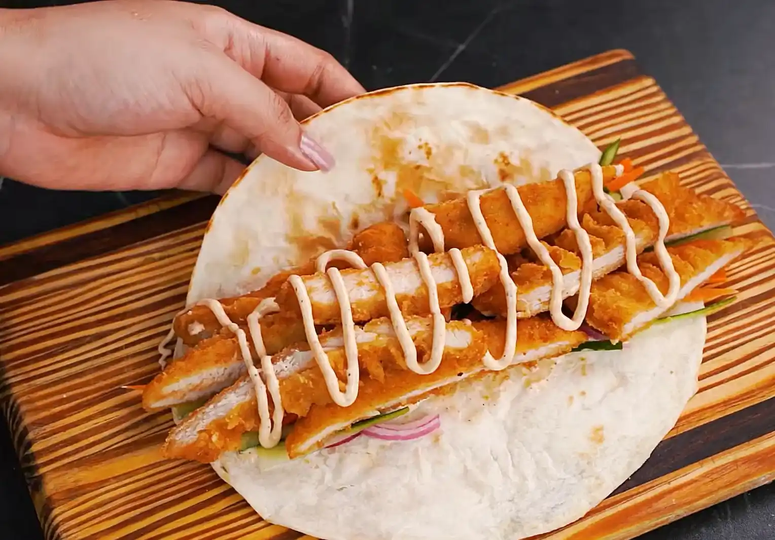 Tortilla layered with pickled vegetables and crispy chicken strips drizzled with spicy mayo before rolling