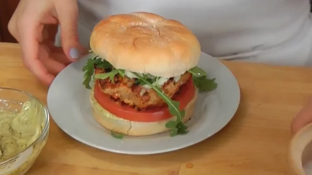 A close-up view of a freshly assembled Caprese turkey burger on a plate, featuring a seasoned turkey patty, fresh mozzarella, ripe tomato slices, fresh basil leaves, and greens on a white bun, served with a side of pesto.