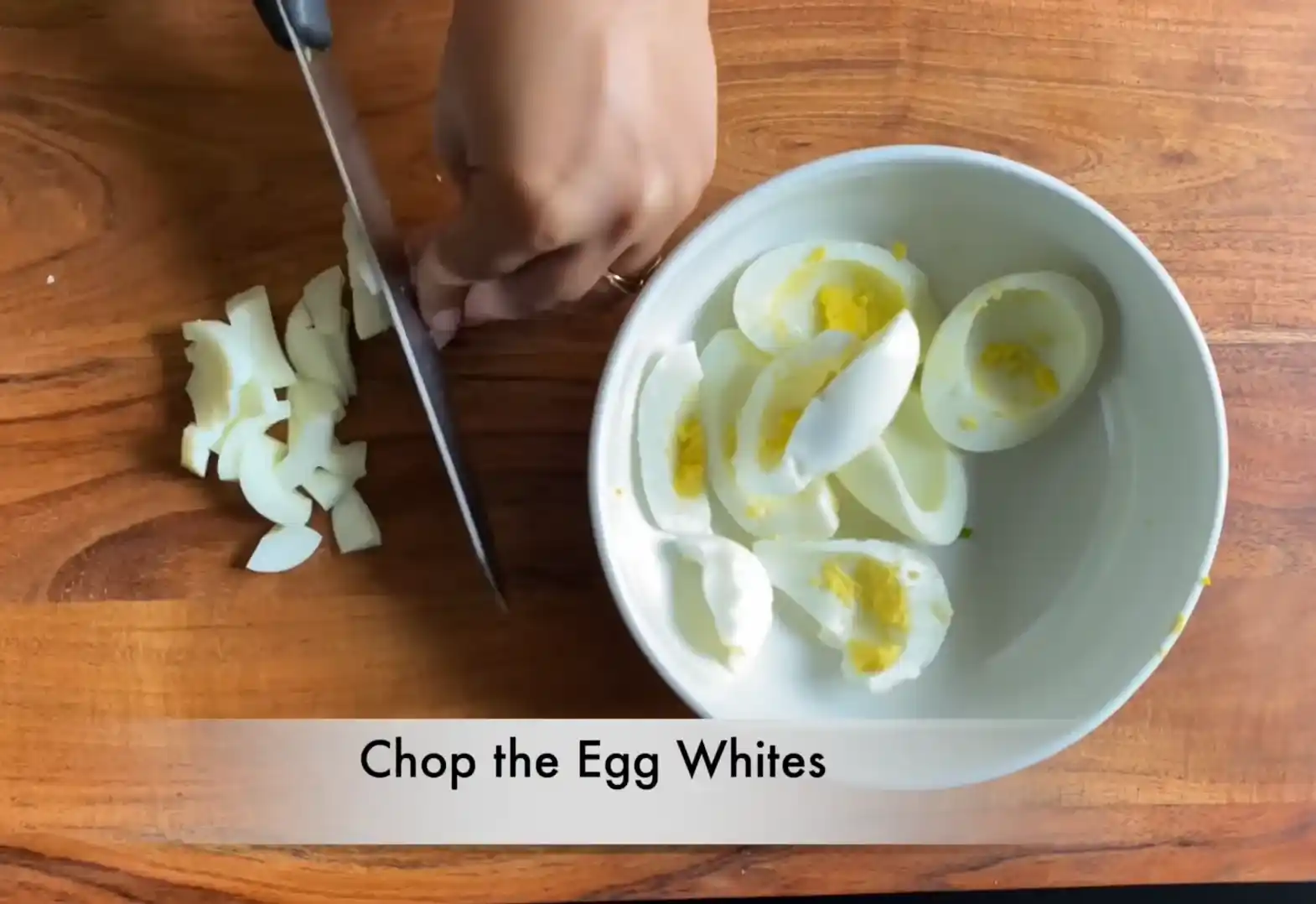 Chef chopping boiled egg whites on wooden cutting board with a sharp knife