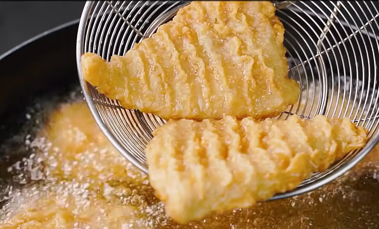 Crispy golden fried chicken fillets being lifted out of hot oil in a metal strainer