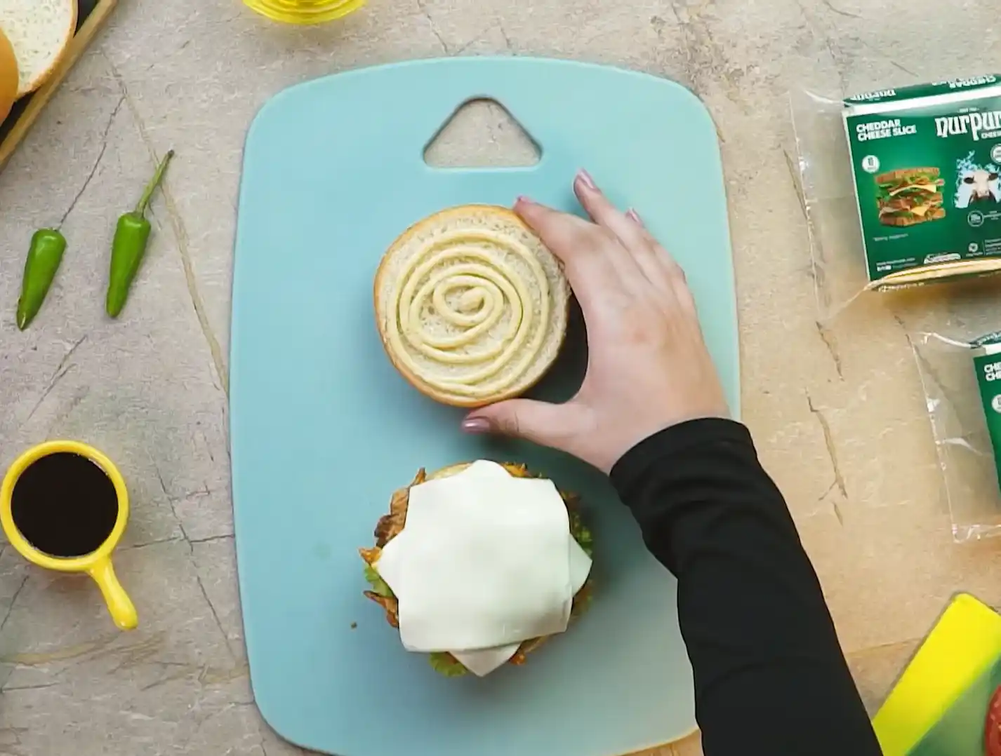 Top bun with mayo swirl being placed on BBQ cheeseburger