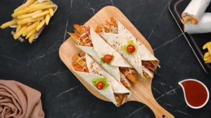 Three crispy chicken wraps sliced in half and garnished with cherry tomato and lettuce skewers on a wooden board