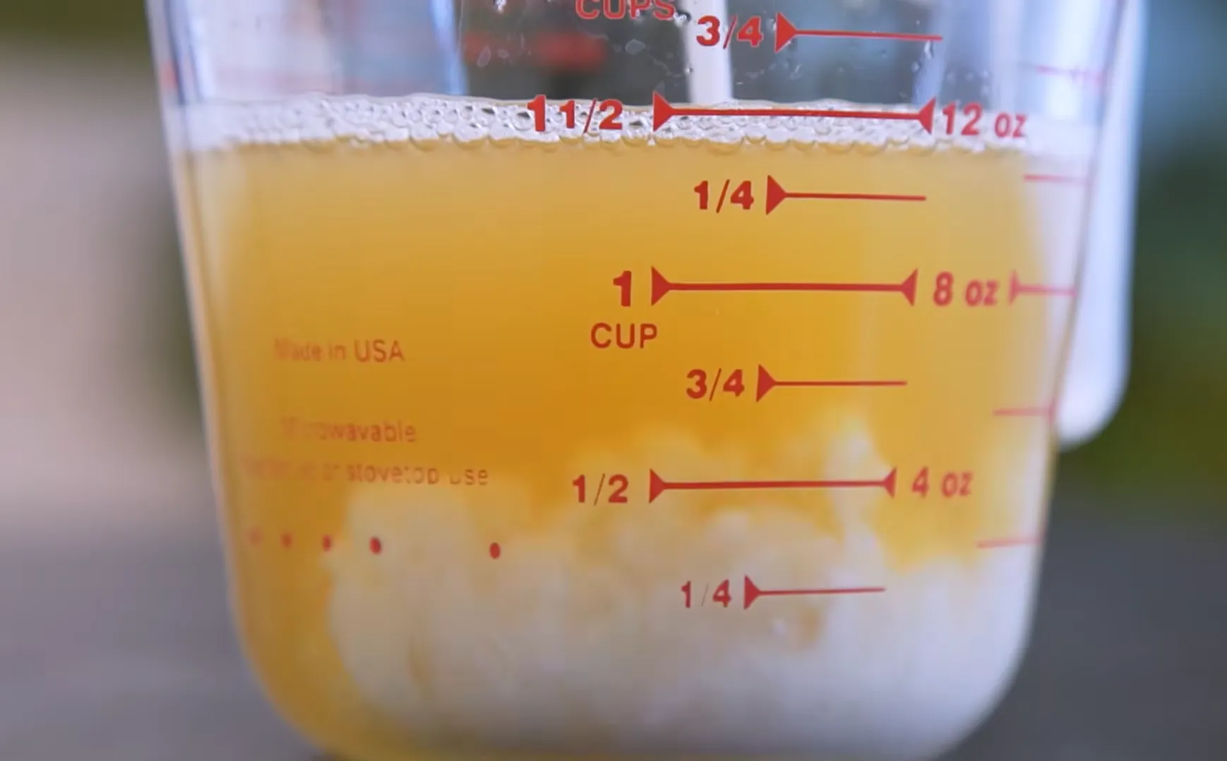 Glass measuring cup showing yellow pineapple refresher juice layer on top and white coconut milk at the bottom