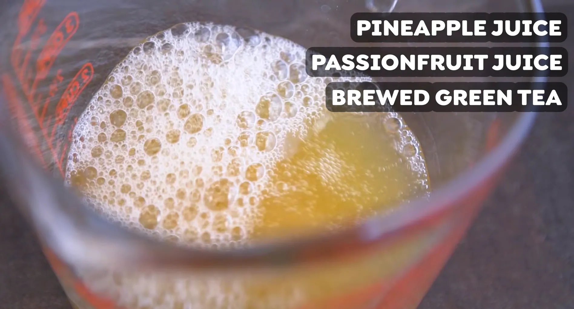 Measuring cup containing pineapple juice, passionfruit juice, and brewed green tea mixture with micro foam