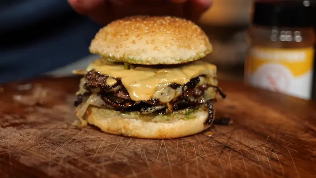 A close-up view of a freshly cooked pit-master smash burger, featuring a crispy caramelized beef patty, melted American cheese, and toppings, served on a toasted sesame seed bun on a rustic wooden cutting board.