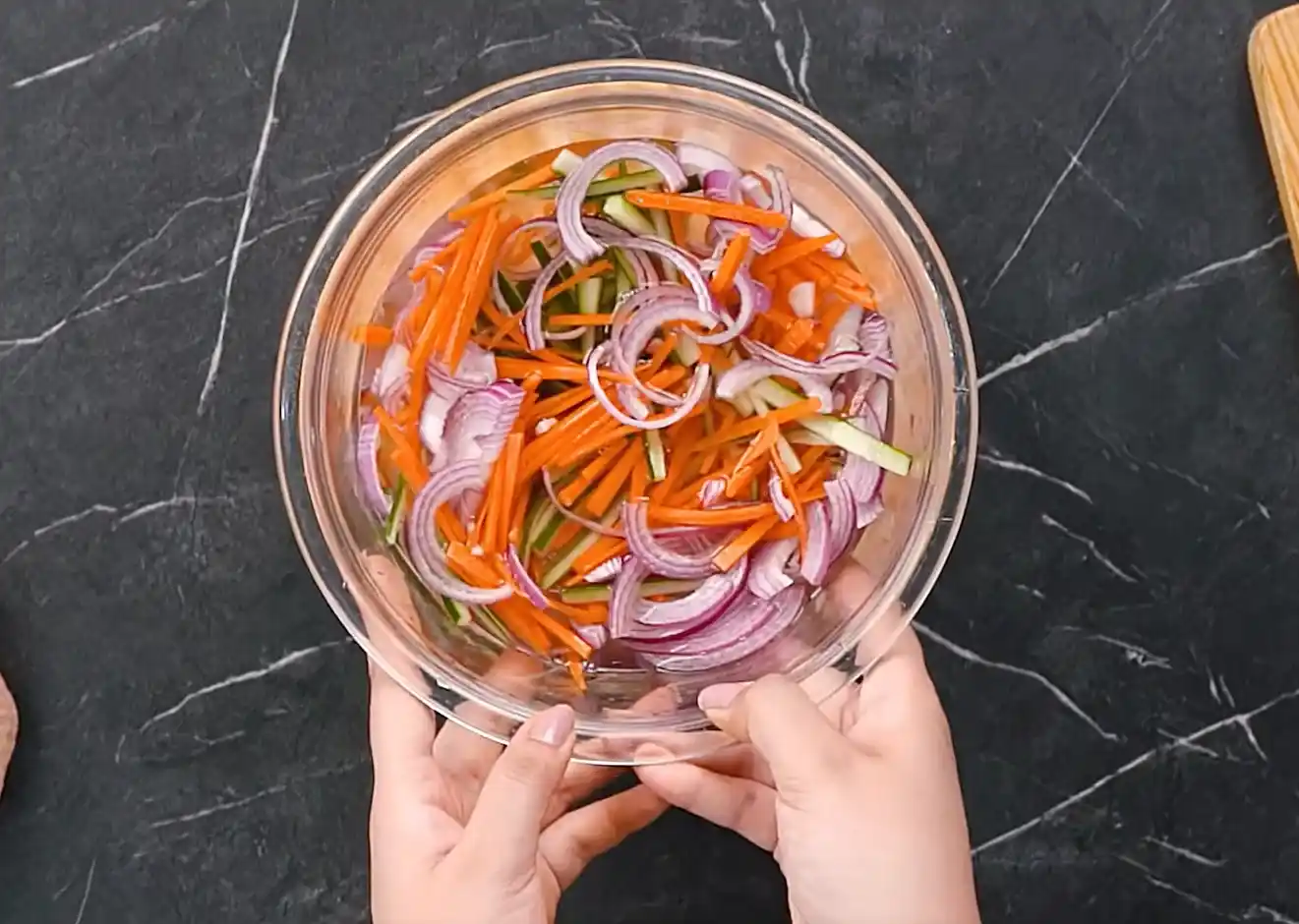 Quick pickled cucumber, carrot, and red onion soaking in vinegar brine in a glass bowl