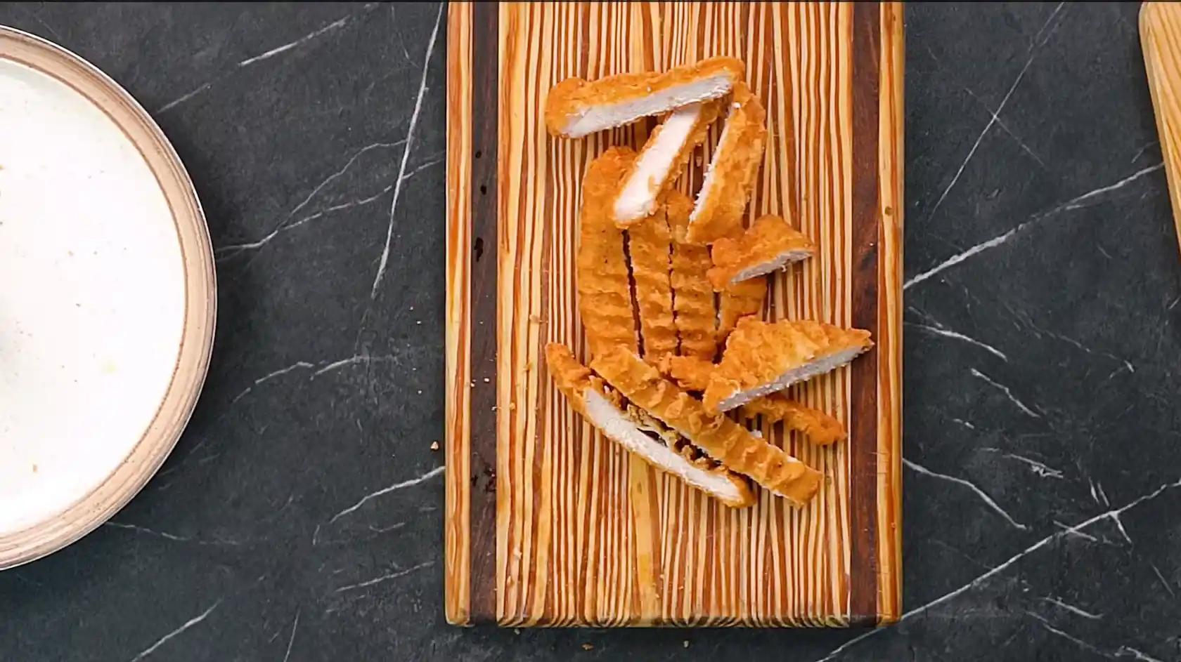 Crispy fried chicken fillet sliced into strips on a wooden cutting board