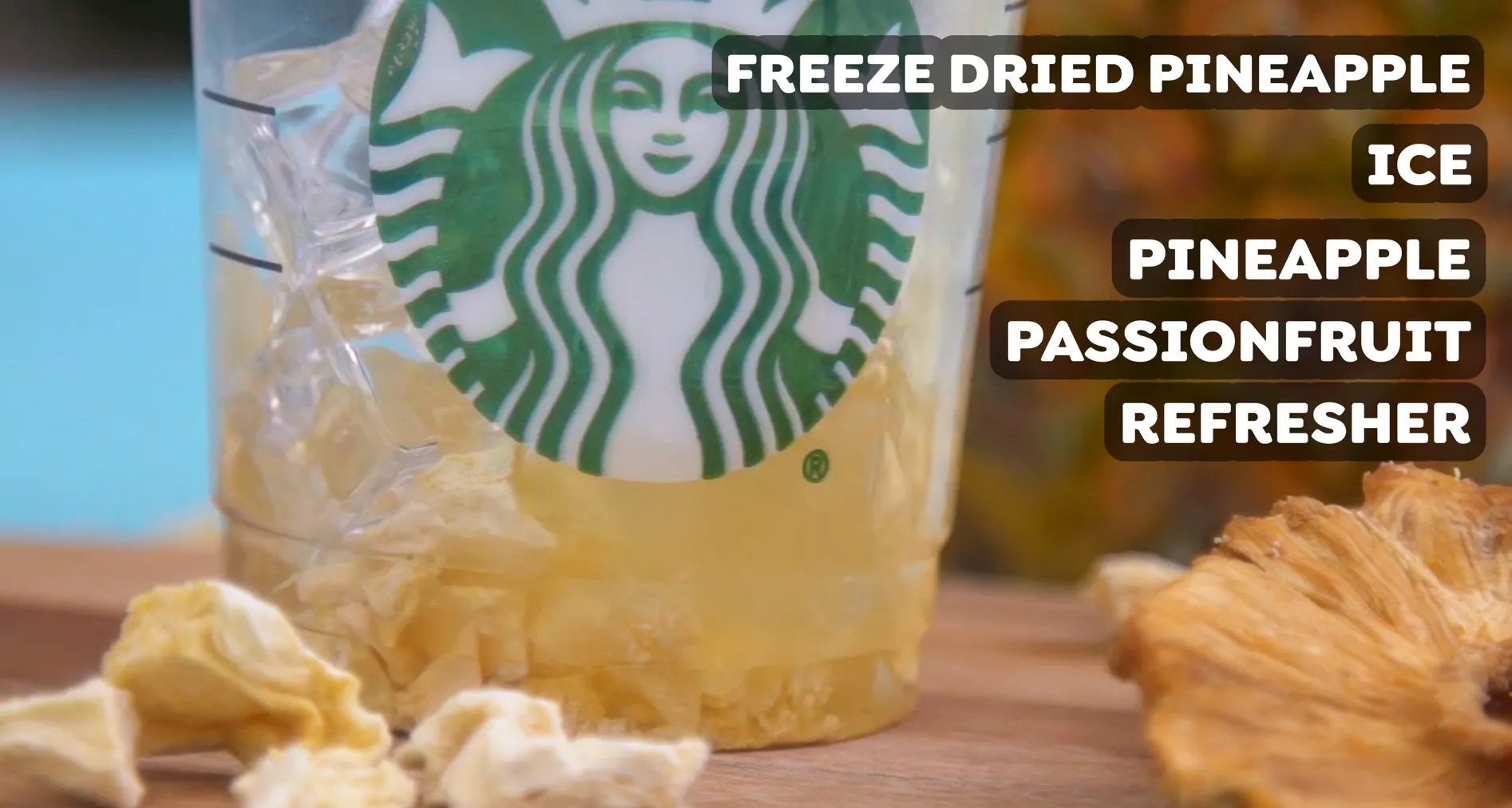 Clear Starbucks cup filled with ice cubes, freeze dried pineapple chunks, and golden passionfruit refresher liquid