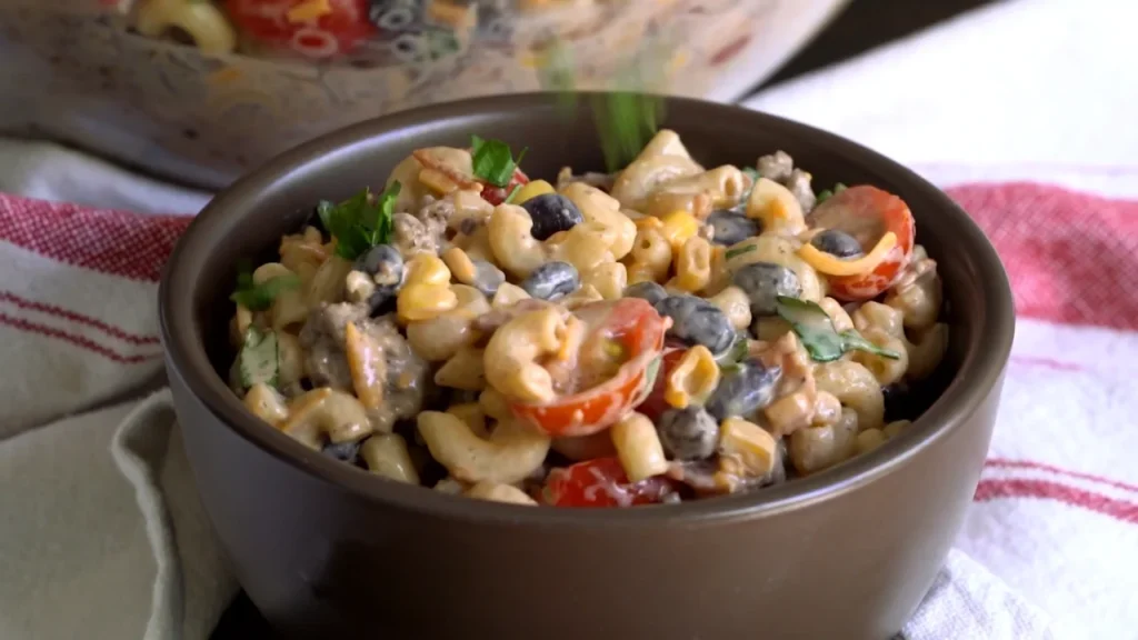 A colorful Tex-Mex cowboy pasta salad made with rotini pasta, corn kernels, black beans, tomatoes, and greens in a smoky dressing.