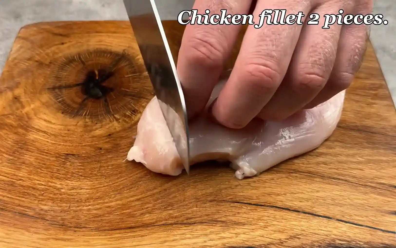 Chef slicing raw chicken breast fillet into strips on wooden board