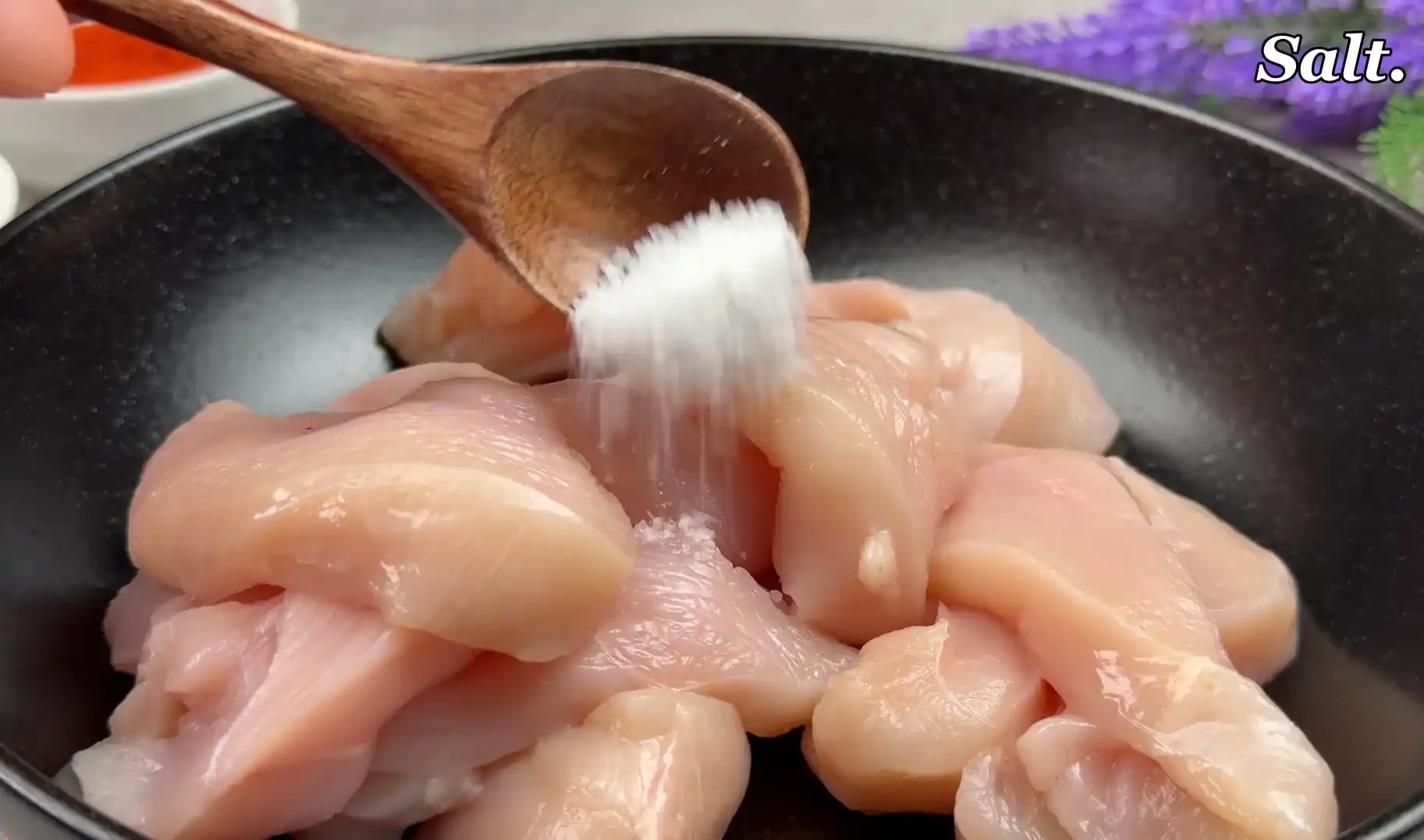 Adding salt to raw sliced chicken breasts in a bowl