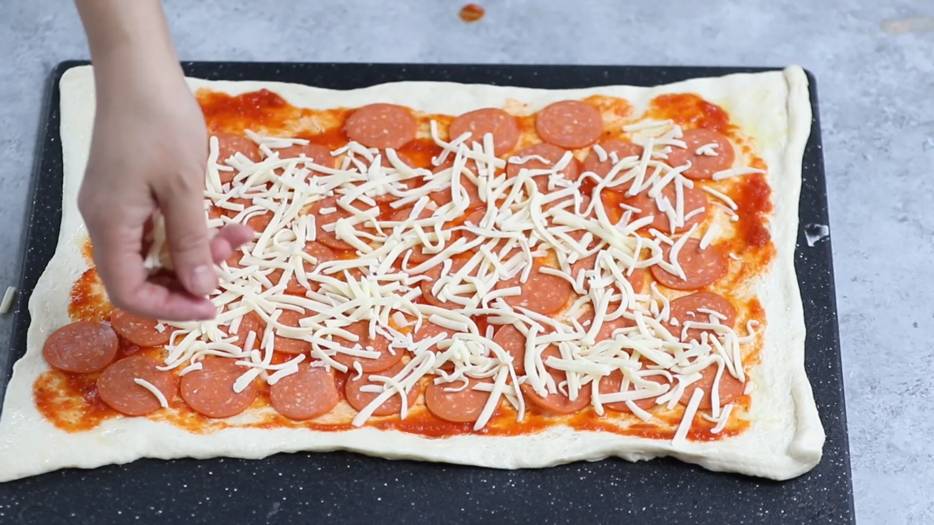 Sprinkling shredded low moisture mozzarella cheese on pepperoni