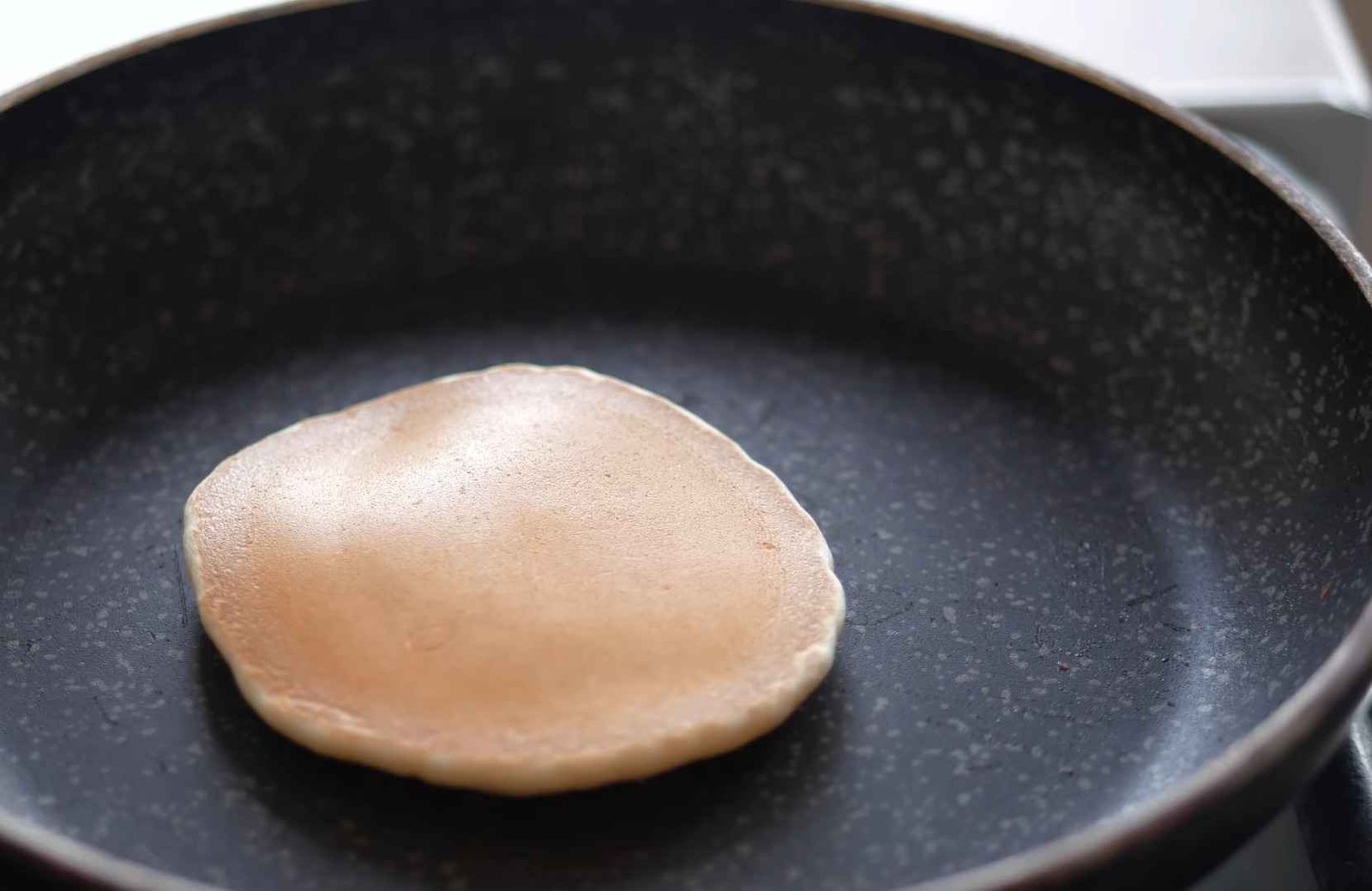 Flipping a pancake in a warm non-stick skillet using a flat spatula showing bubbles popping and a golden brown crust