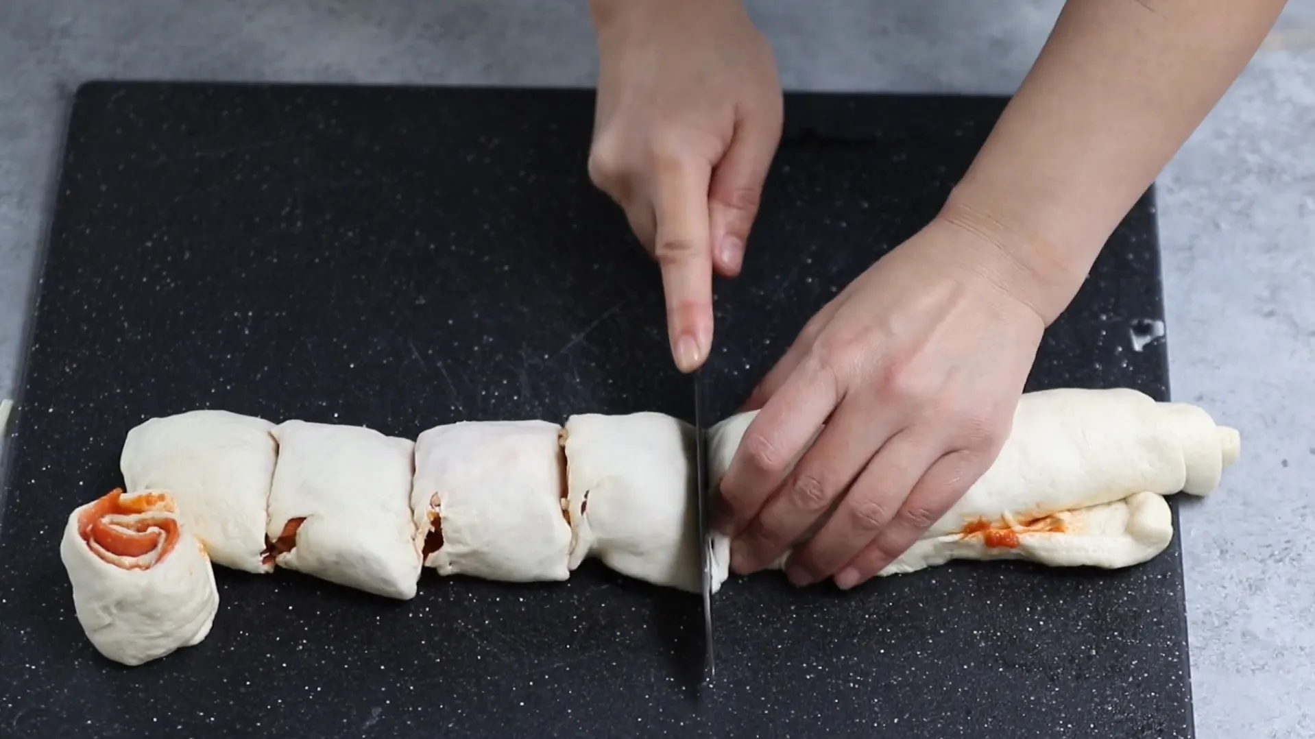 Slicing pizza dough log into individual pinwheels with a sharp knife