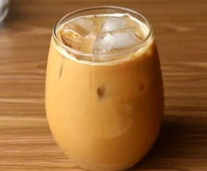 Creamy homemade iced coffee served in a glass tumbler with ice cubes on a wooden table.