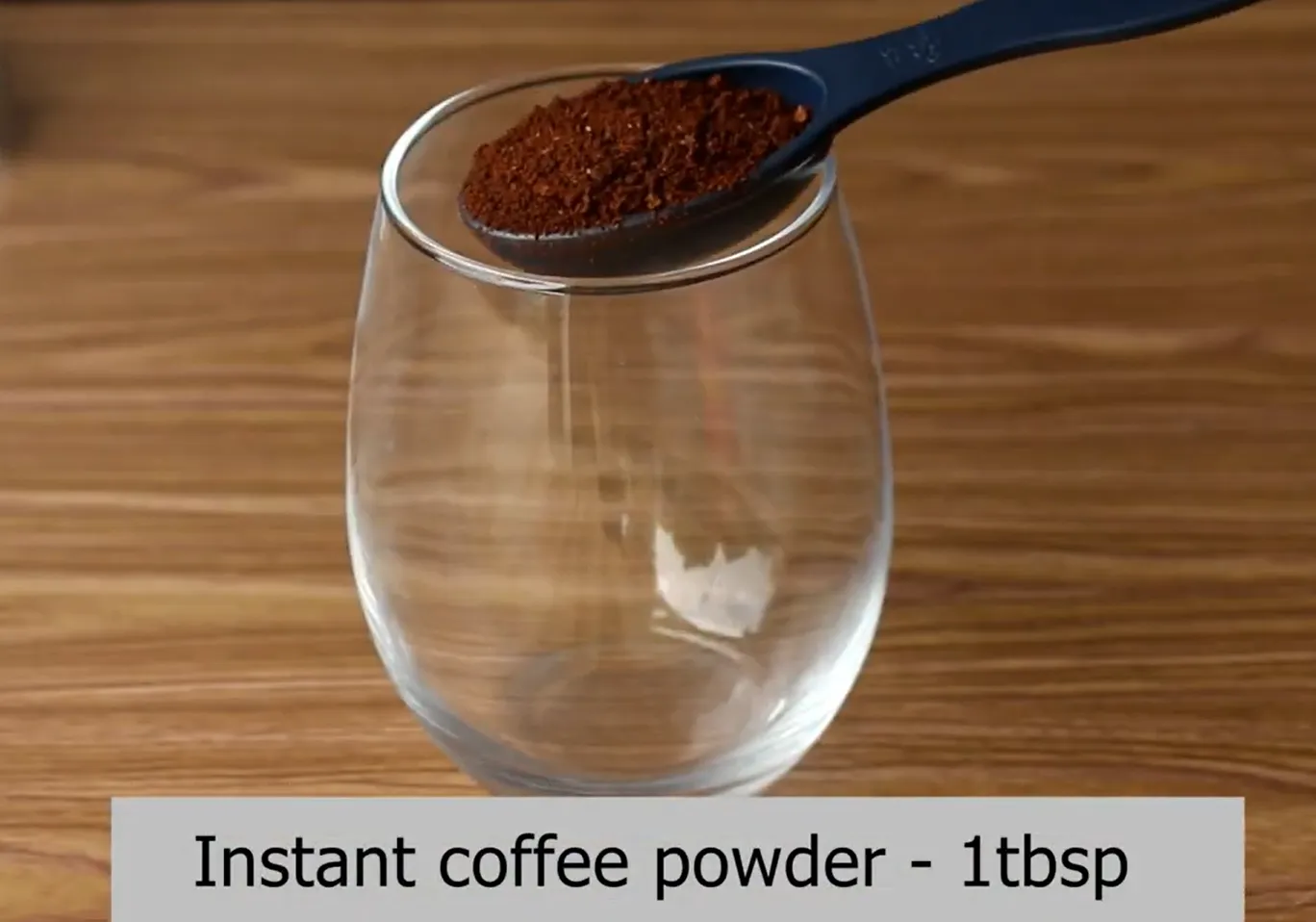 Adding instant coffee powder to a glass tumbler with a measuring spoon.
