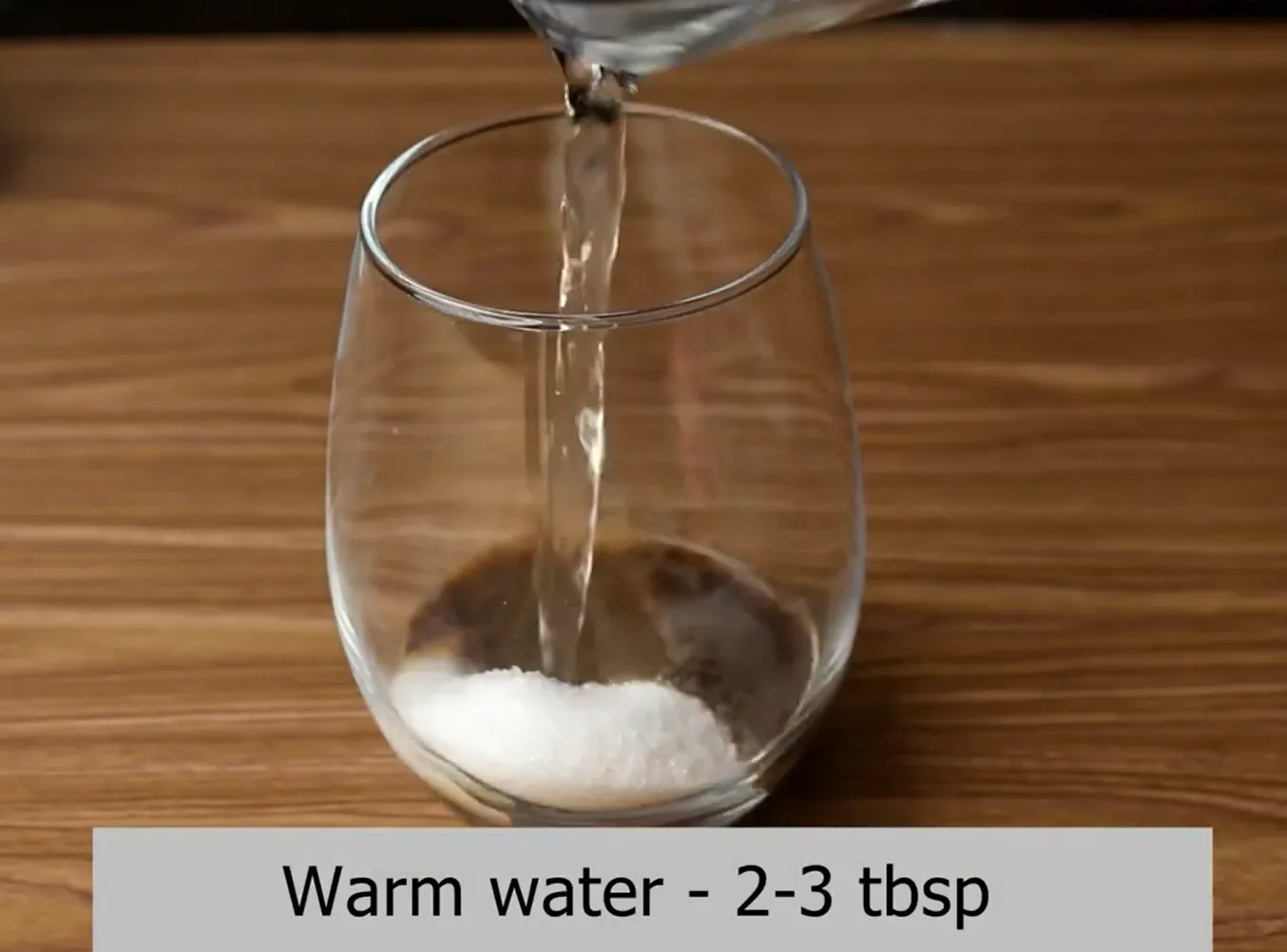 Pouring warm water into a glass with instant coffee and sugar.
