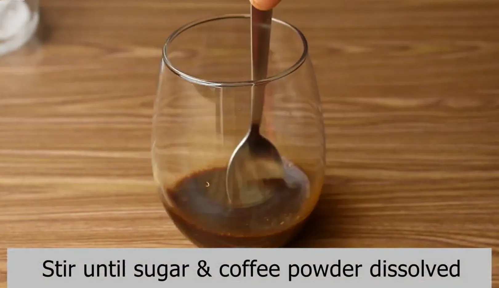 Stirring warm water, sugar, and instant coffee with a spoon to make coffee syrup.