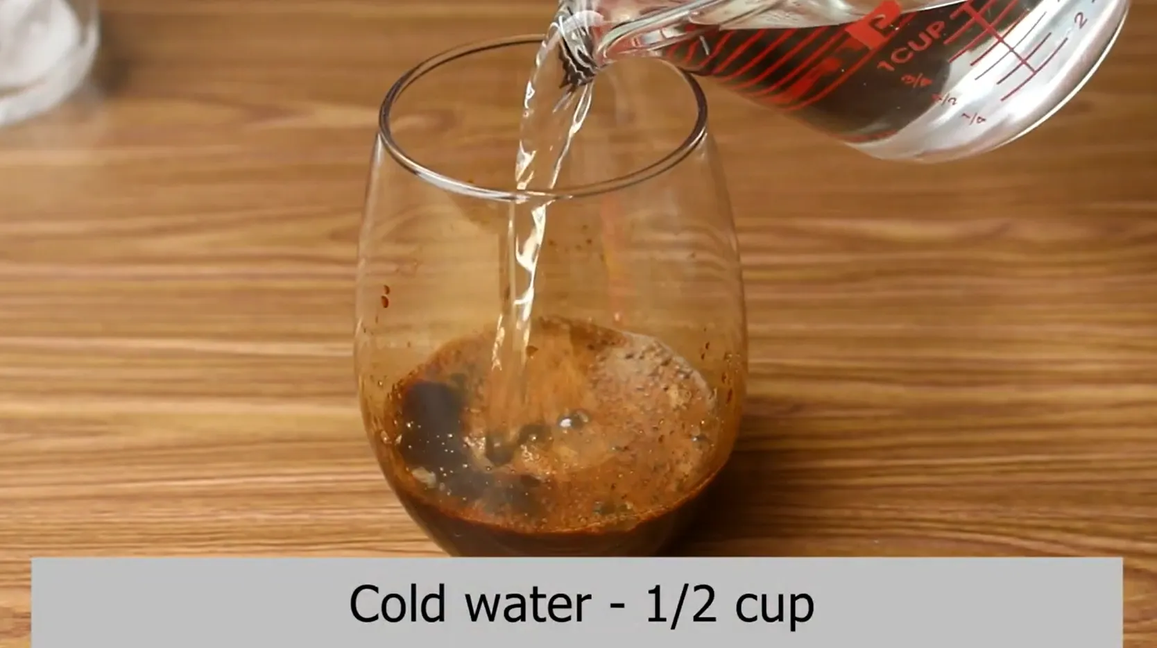 Pouring cold water from a liquid measuring cup into dissolved coffee syrup.