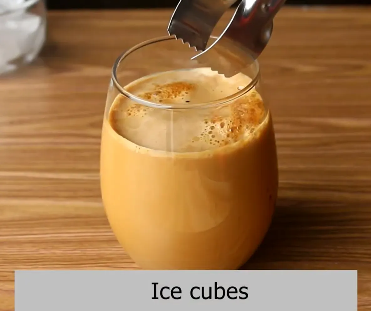 Adding ice cubes using tongs into a glass of homemade iced coffee and stirring to serve.