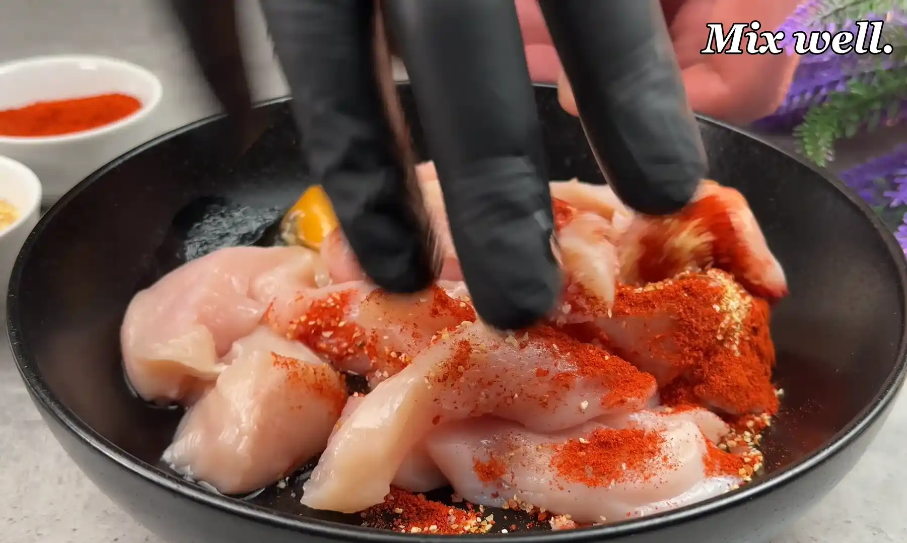Mixing spices and egg into chicken strips with black gloved hands