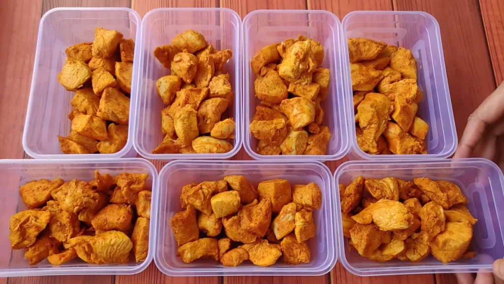 Eight plastic meal prep containers filled with portioned, seasoned cooked chicken breast cubes.