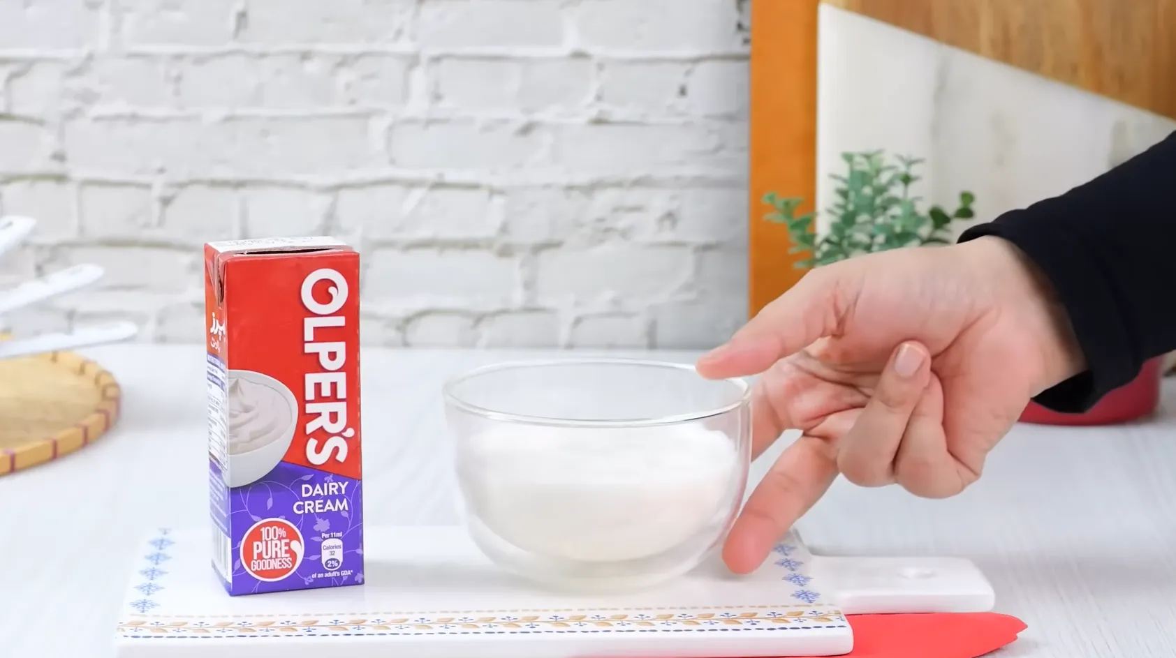 A pack of Olper's Dairy Cream next to a bowl of liquid cream on a white background.