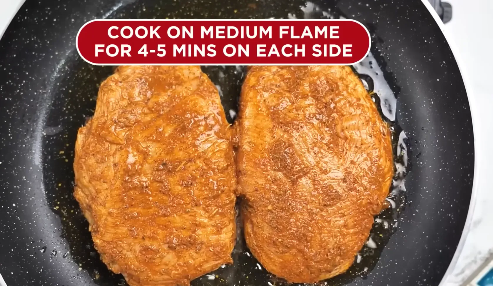 Searing two marinated chicken breasts in a hot black skillet on medium flame.