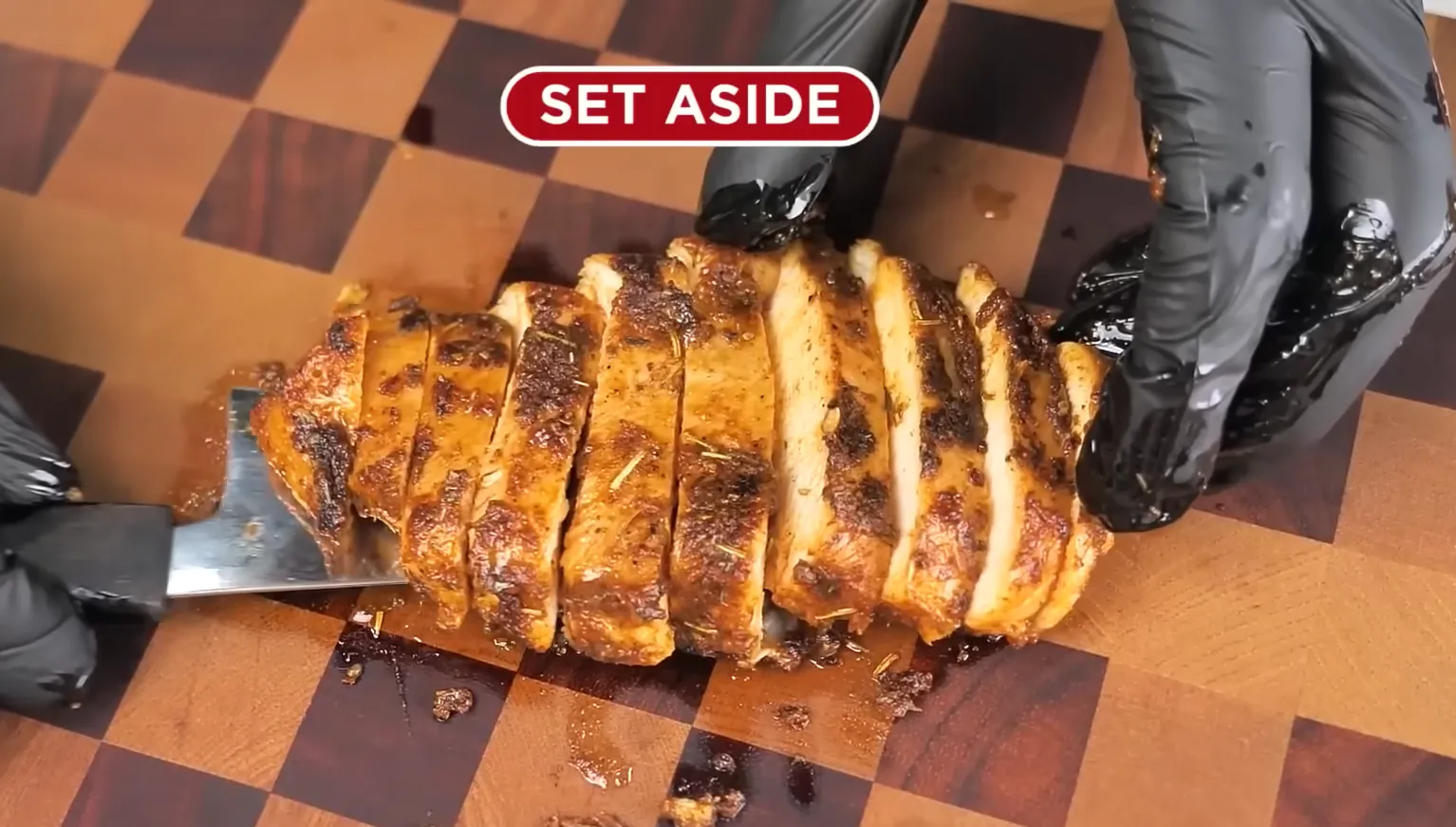Sliced grilled chicken breast being held with a spatula on a wooden cutting board with a Set Aside label.