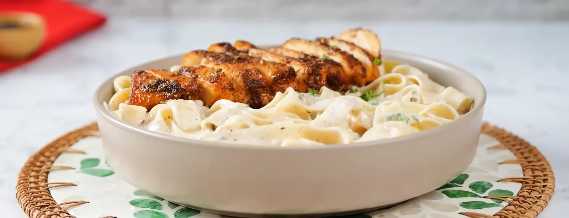 A beautiful bowl of restaurant-style Chicken Alfredo Pasta served on a woven placemat.