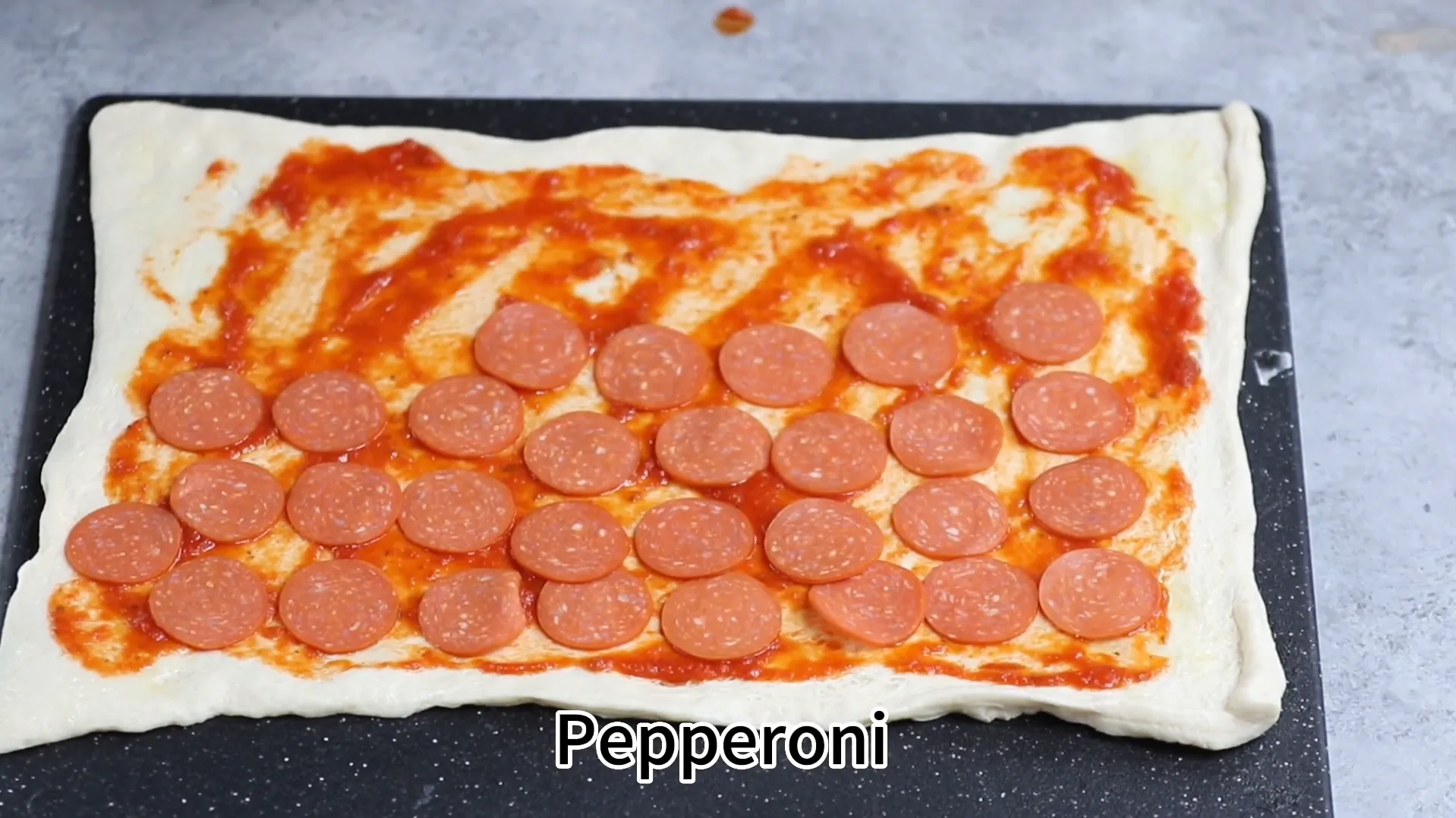 Layering sliced pepperoni on top of pizza sauce layer