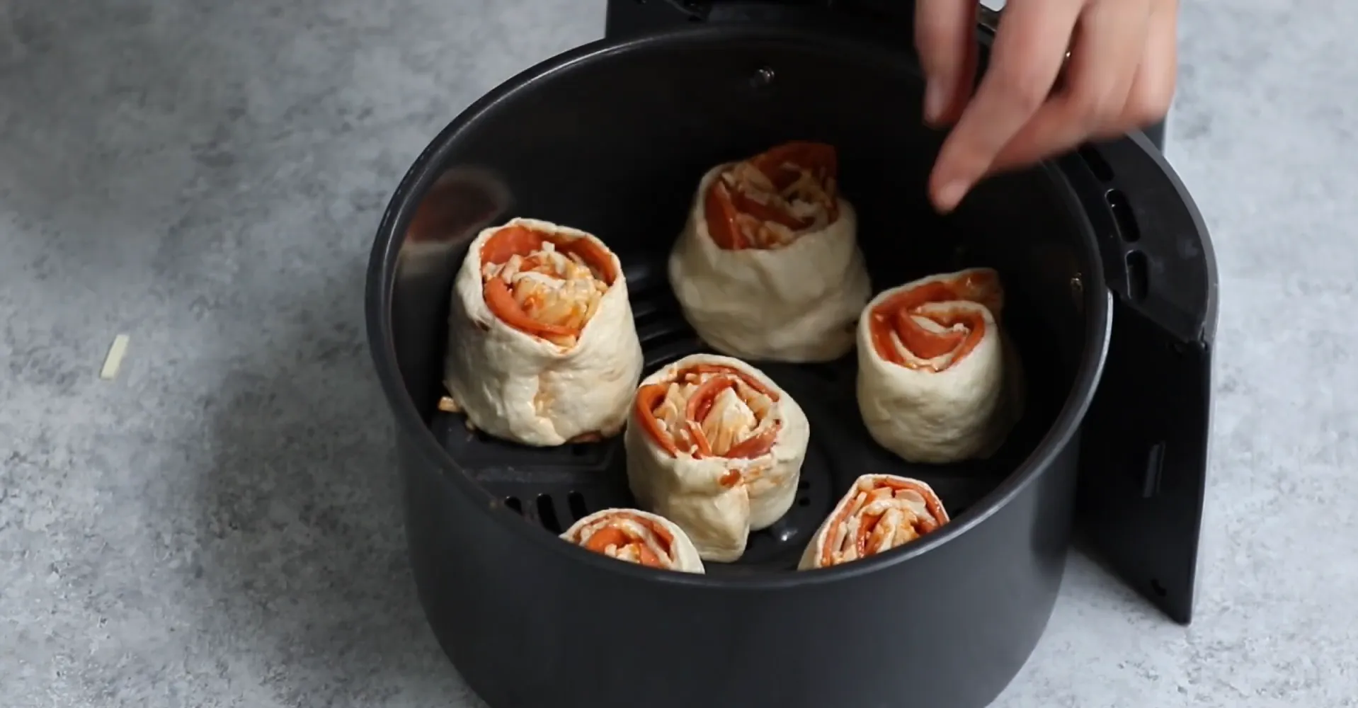 Arranging raw pizza pinwheels in air fryer basket with spacing