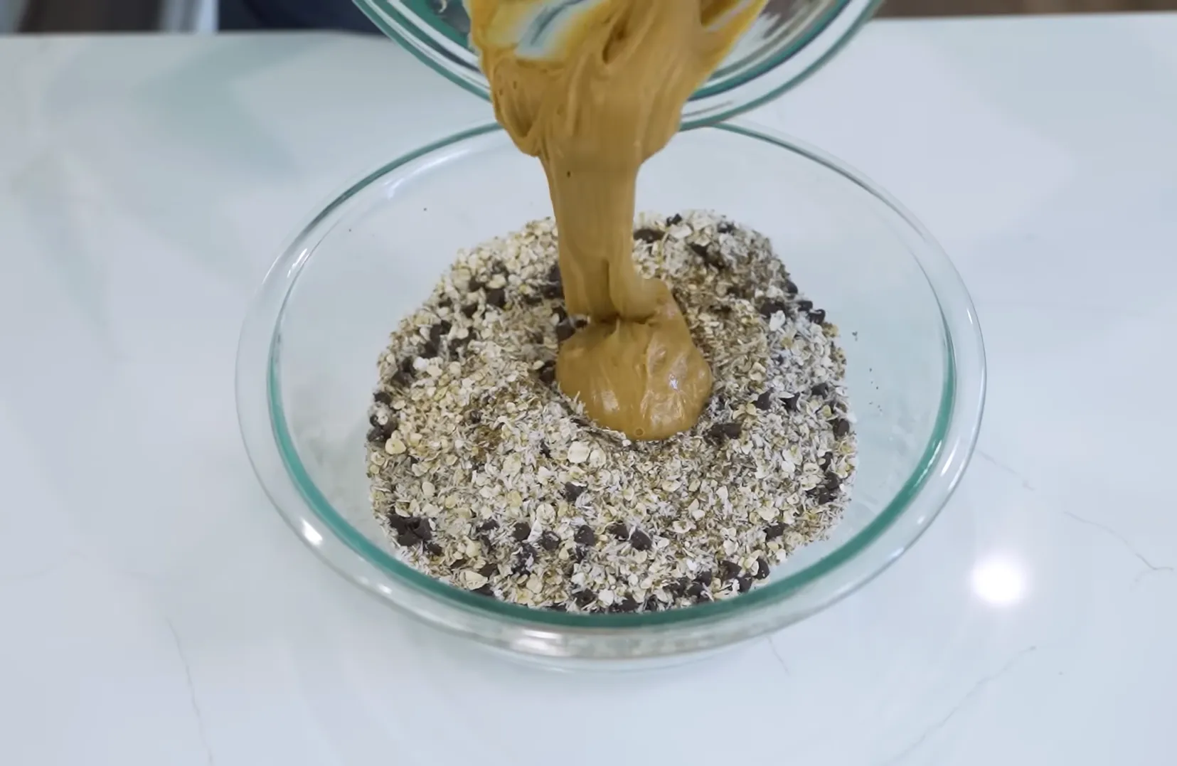 Pouring creamy peanut butter into oat and chocolate chip mixture for no-bake energy bites