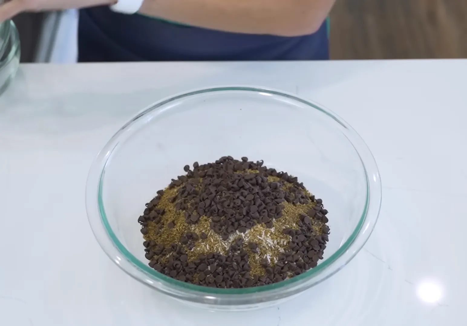 Glass bowl containing dry ingredients for oat energy balls including oats and mini chocolate chips