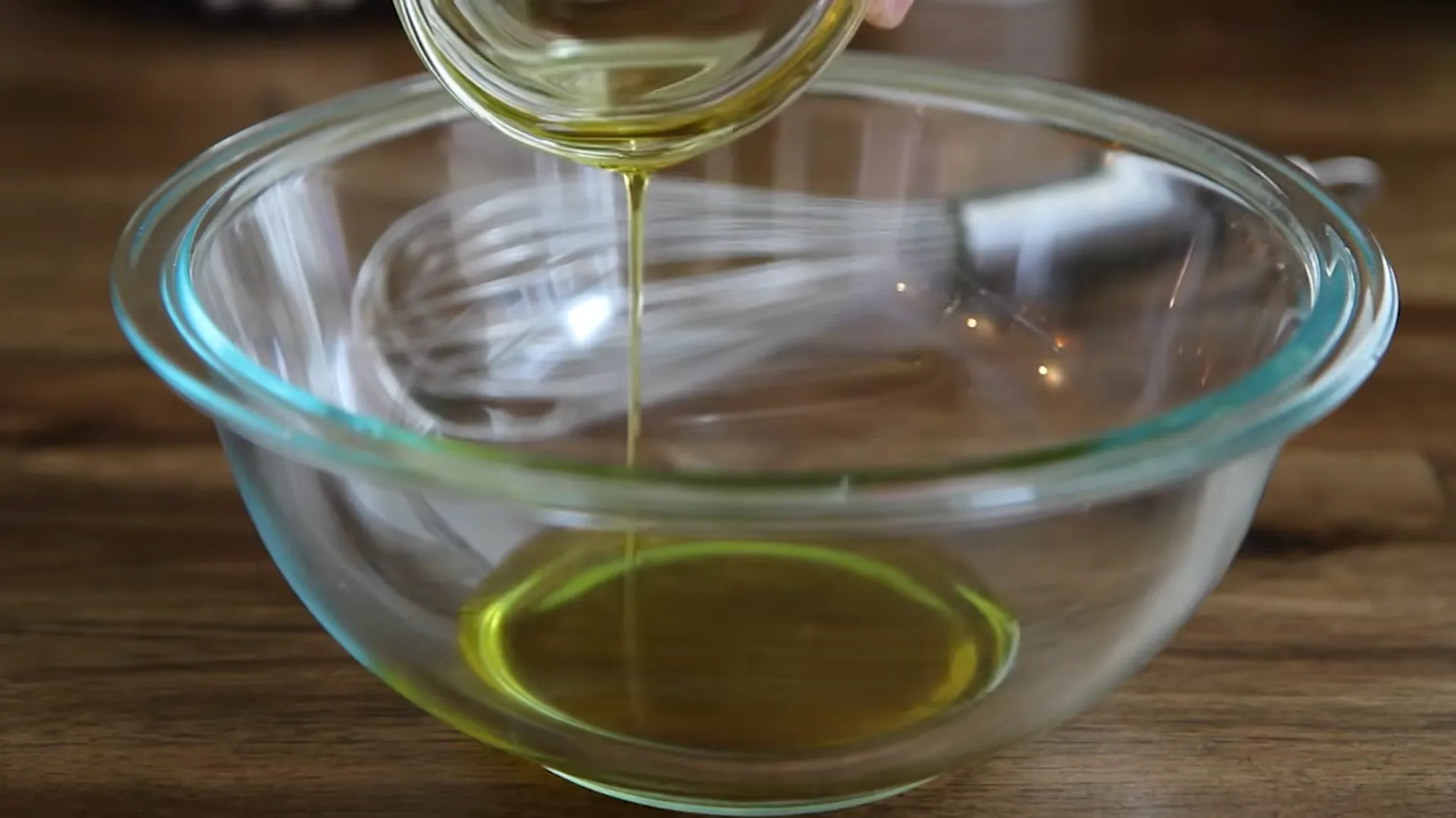 Pouring extra virgin olive oil into a glass bowl as the base for a homemade steak marinade recipe
