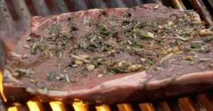 Marinated beef steak grilling over high heat with garlic and fresh rosemary on BBQ grates