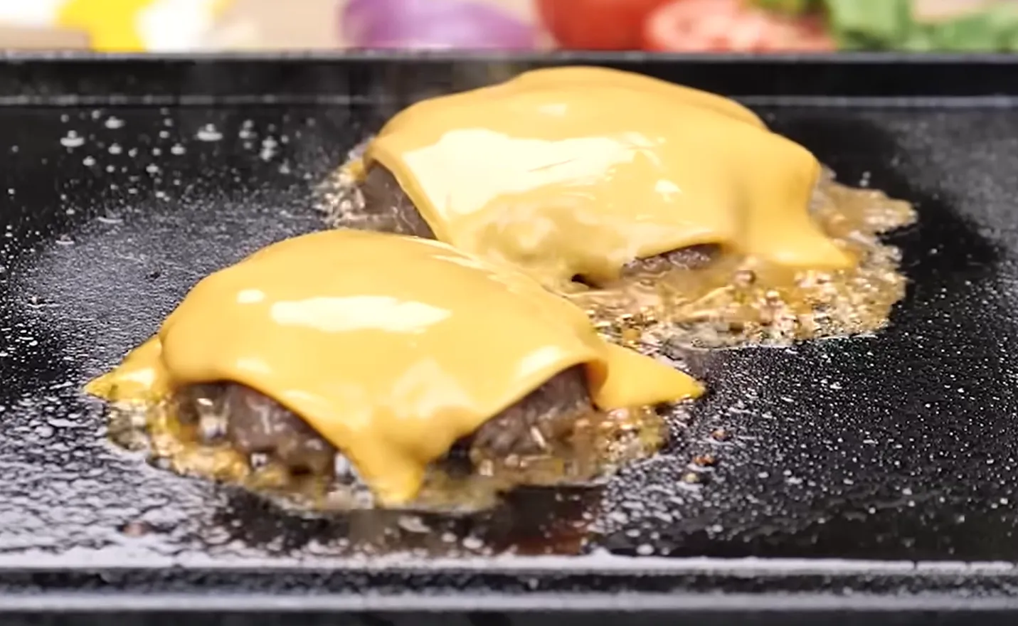 Cheddar cheese melting over smash burger patties on a griddle