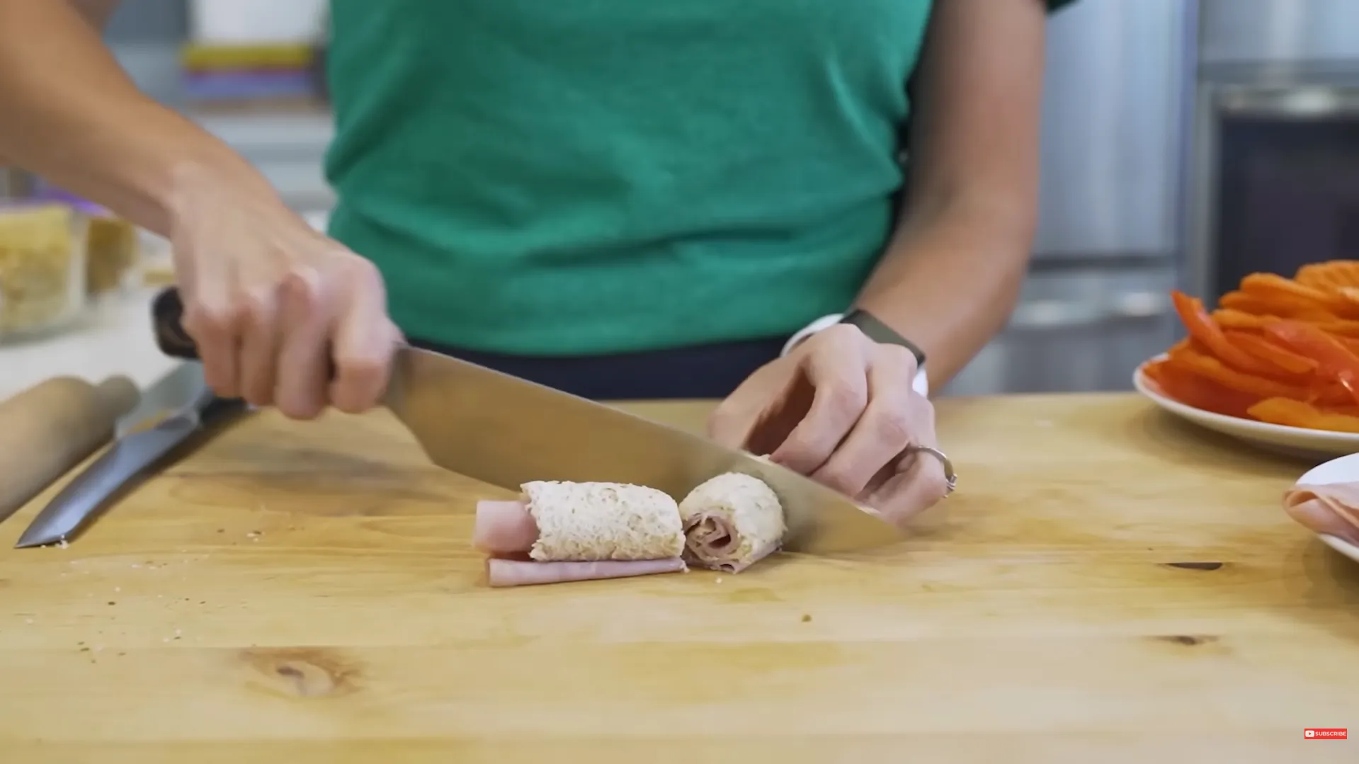 Chef slicing homemade ham and cream cheese sandwich roll ups on a wooden cutting board